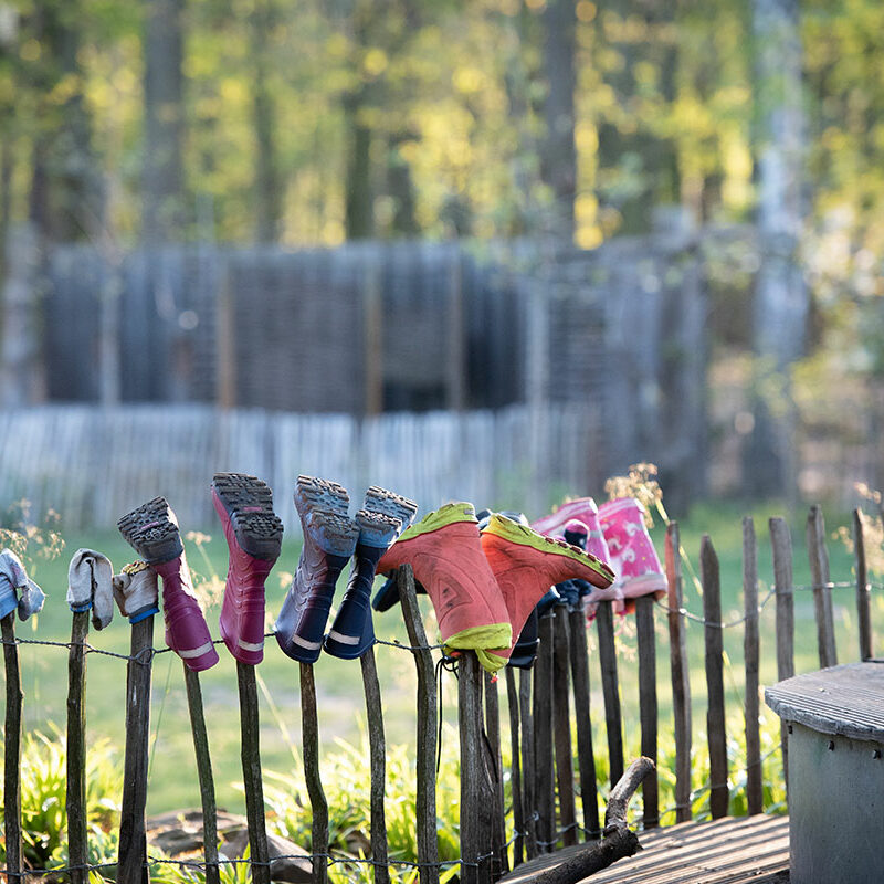 Gummistiefel und Socken von Kindern, die über einen Holz-Gartnezaun zum trocknen aufgehangen wurden.