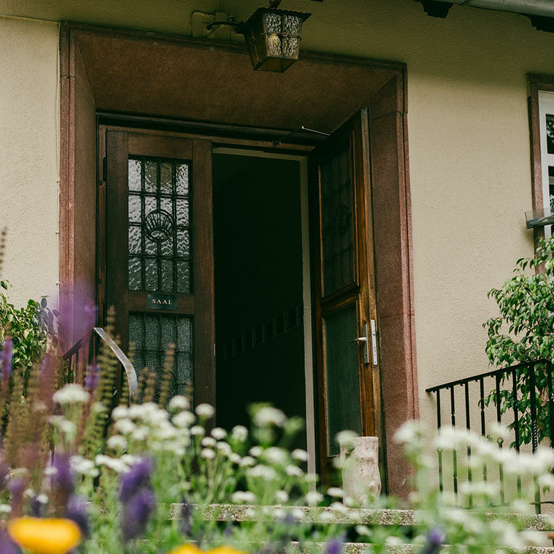 Alte, klassische Eingangstür zum Naturfreundehaus. Unscharf im Vordergrund sind bunte Wiesenblumen.