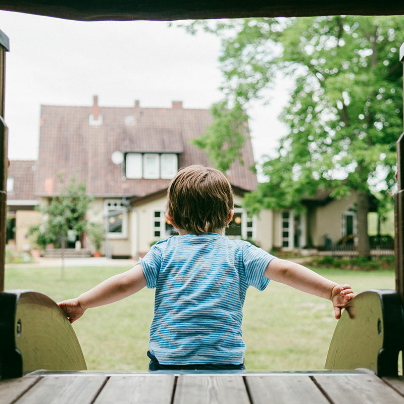 Ein Kind auf der Rutsche im Garten. Im Hintergrund das Naturfreundehaus Hannover.