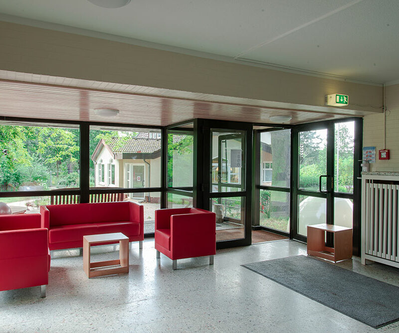 Kleine Sitzecke mit zwei Sesseln und einem Sofa vor Fensterfront.